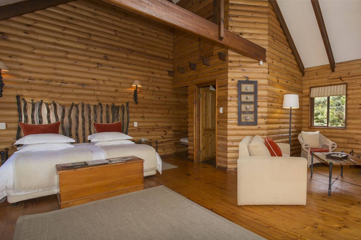 A log cabin bedroom with a wooden bed, two bedside lamps, a sofa, and a fireplace.