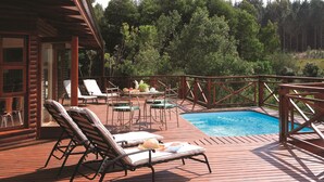 Una terraza de madera con sillones de descanso, una piscina pequeña y una mesa con sillas.