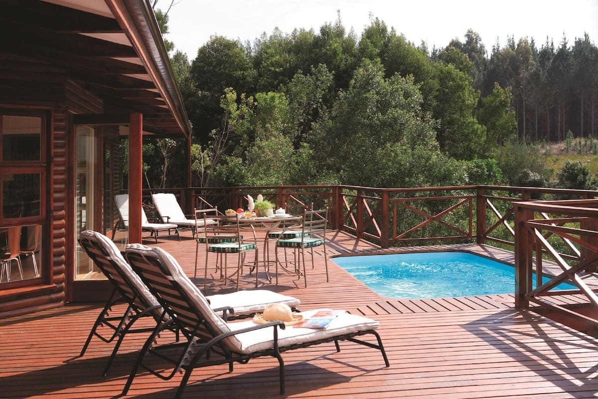 A wooden deck with lounge chairs, a small pool, and a table with chairs.