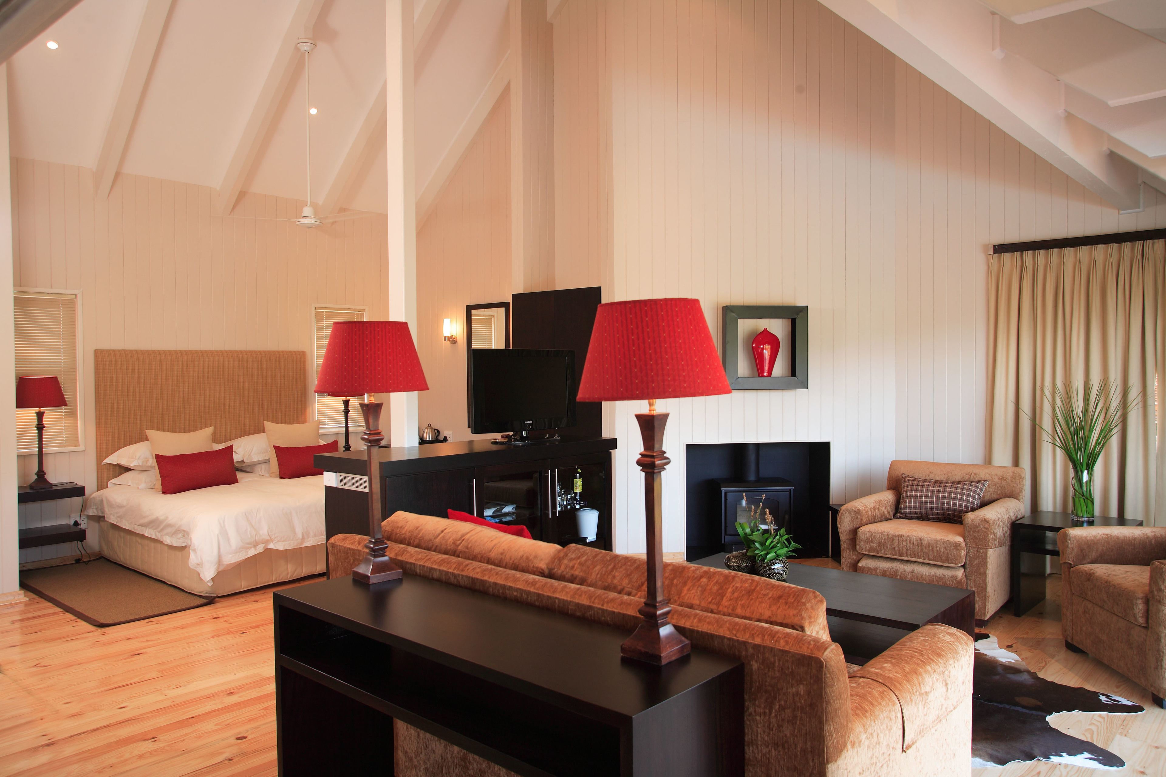 A modern hotel room with a bed, a sofa, a coffee table, and a fireplace.