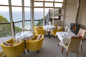 A dining area with yellow chairs and tables set for two, overlooking a scenic ocean view. -  The Fernery Lodge and Spa  (Storms River)