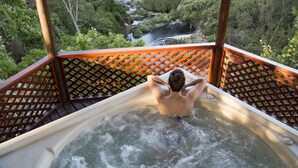 Una persona relajándose en un jacuzzi con vistas a un área boscosa y un arroyo.