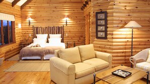 Interior de una cabaña de troncos con una cama, dos sofás, una mesa de centro y una lámpara.