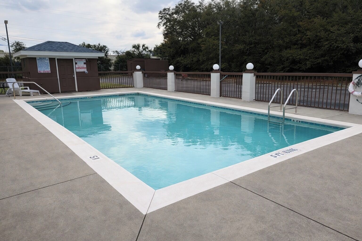 Una piscina rectangular con una escalera metálica y una cerca con remates esféricos.