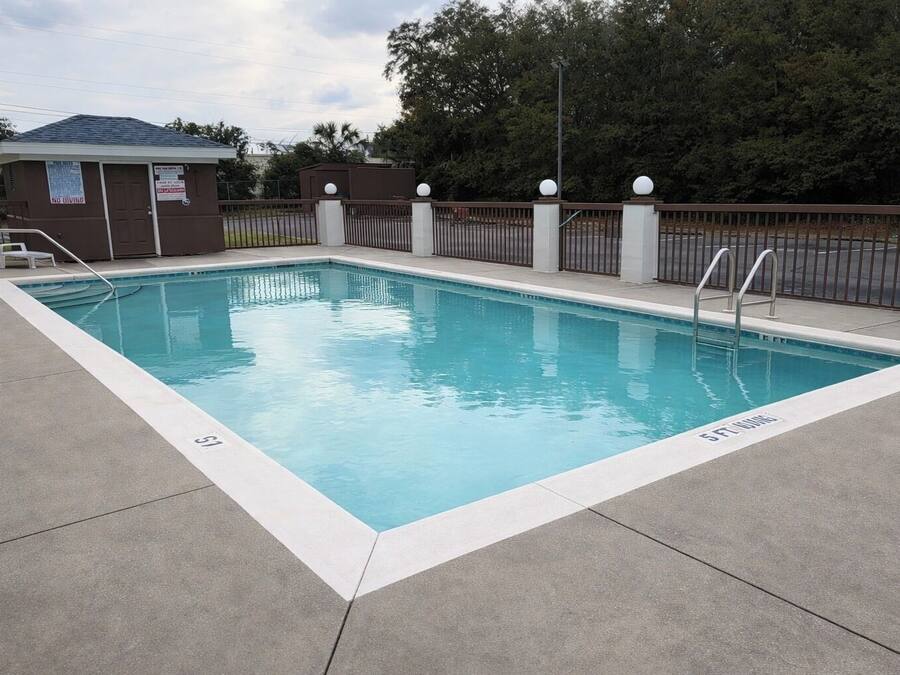 Una piscina rectangular con una escalera metálica y una cerca con remates esféricos.