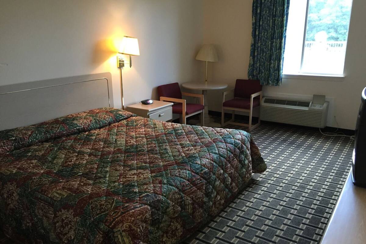 Una habitación de hotel con cama, escritorio, silla, lámpara y ventana.