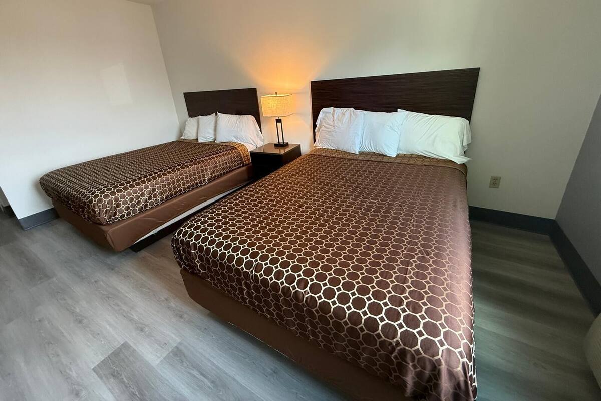Habitación de hotel con dos camas individuales y una cama más grande, todas con ropa de cama de estampado marrón.