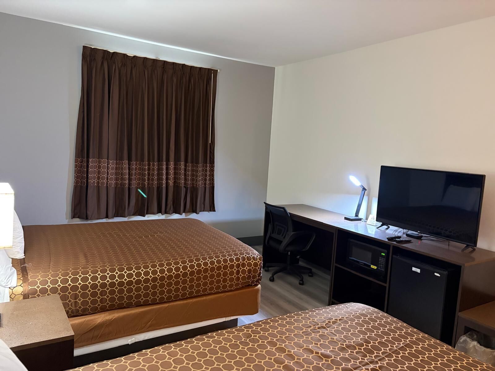 Habitación de hotel con dos camas, un escritorio con computadora y televisión, y un refrigerador pequeño.