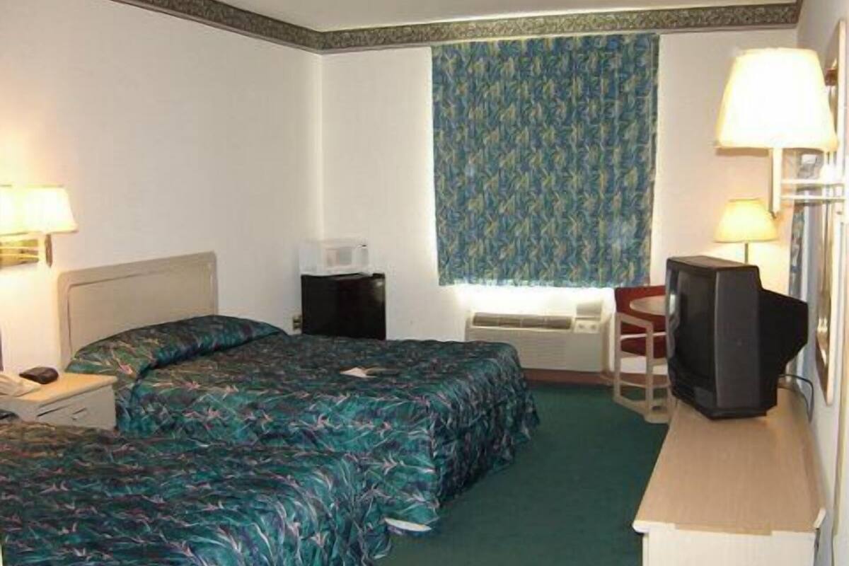 Habitación de hotel con dos camas, un escritorio con televisor, una silla, una lámpara de escritorio, microondas y una ventana con cortinas estampadas.