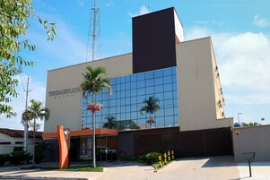 A modern hotel with a large glass facade, palm trees, and a clear blue sky.