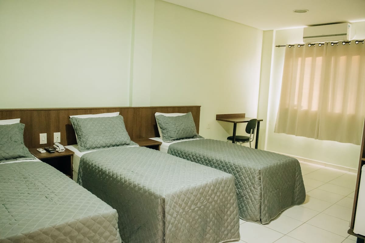 A hotel room with three beds, a desk, a chair, and an air conditioning unit.