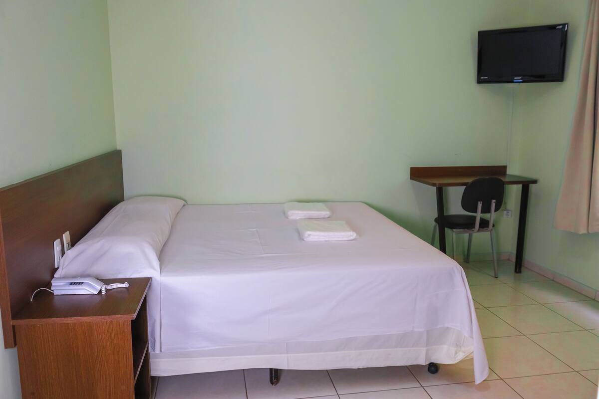 A hotel room with a bed, a desk, a chair, and a TV mounted on the wall.