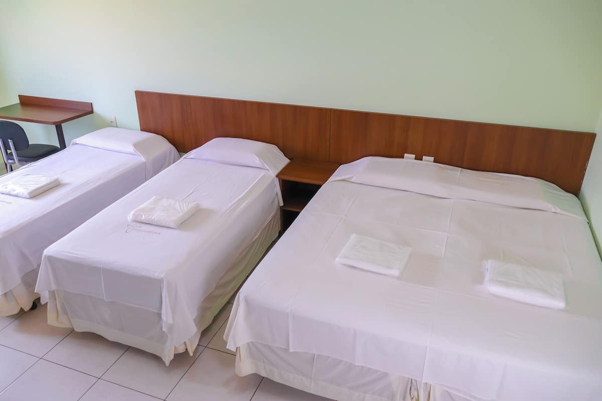 A hotel room with two single beds, a wooden headboard, a small table, and a chair.