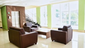 A spacious lobby with a staircase, brown leather sofas, a wooden coffee table, and large windows with a view of greenery. - Trindade Plaza Hotel (Trindade)