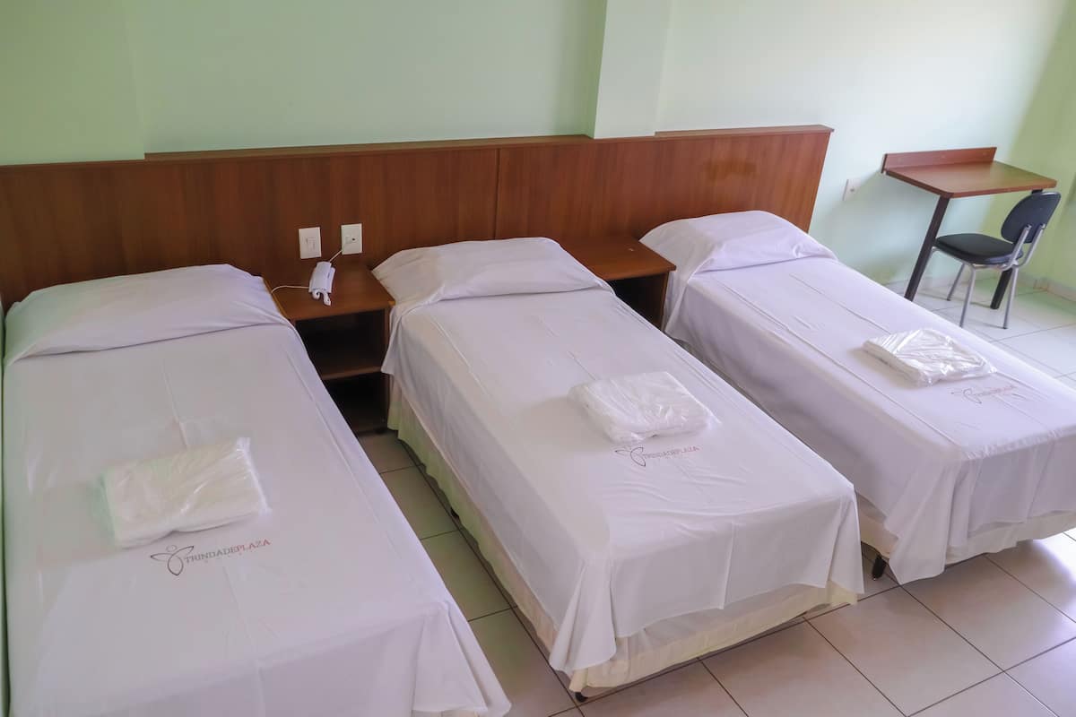A hotel room with three single beds, a wooden headboard, a small wooden table, and a chair.