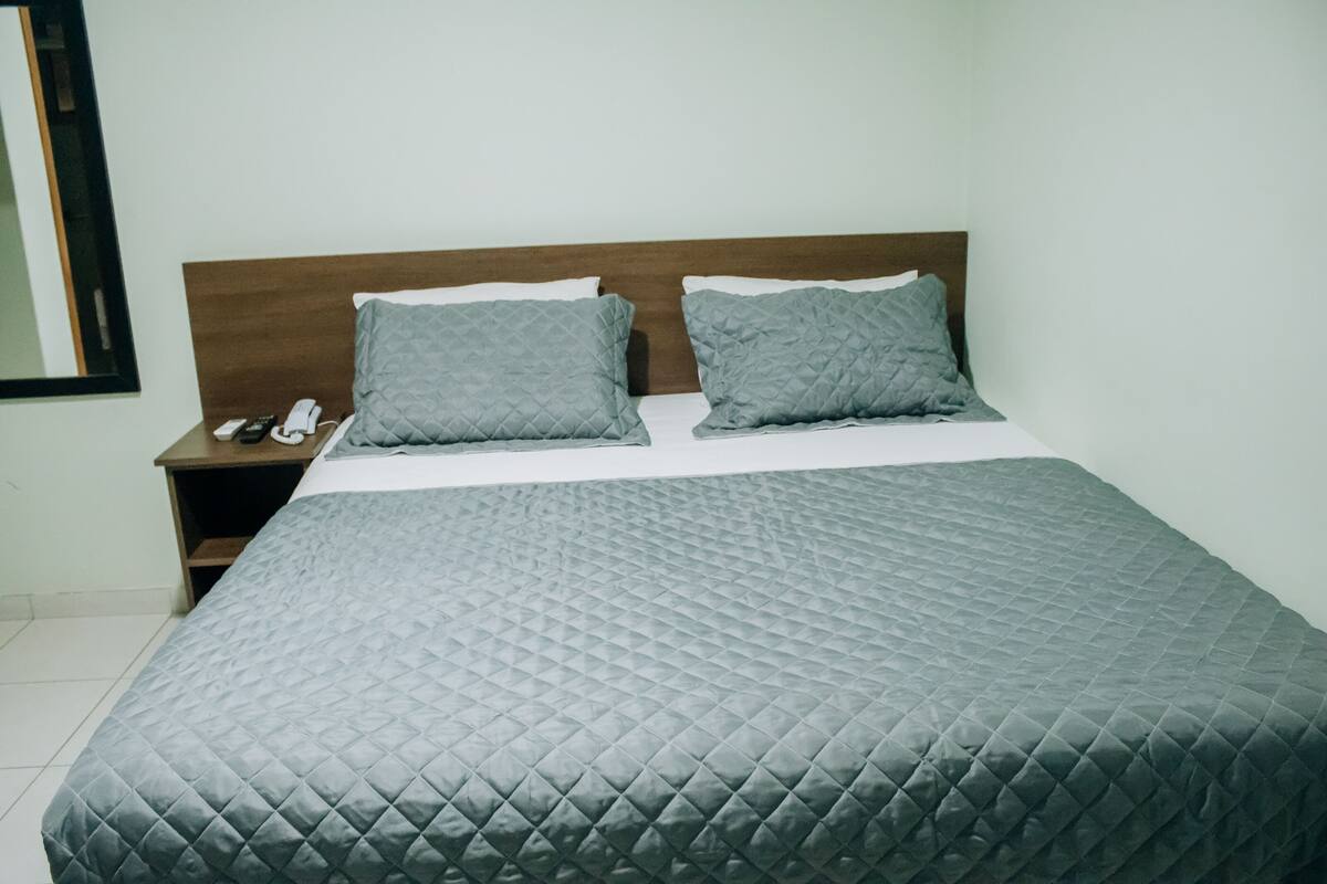 A neatly made bed with a quilted cover, two pillows, and a wooden headboard.