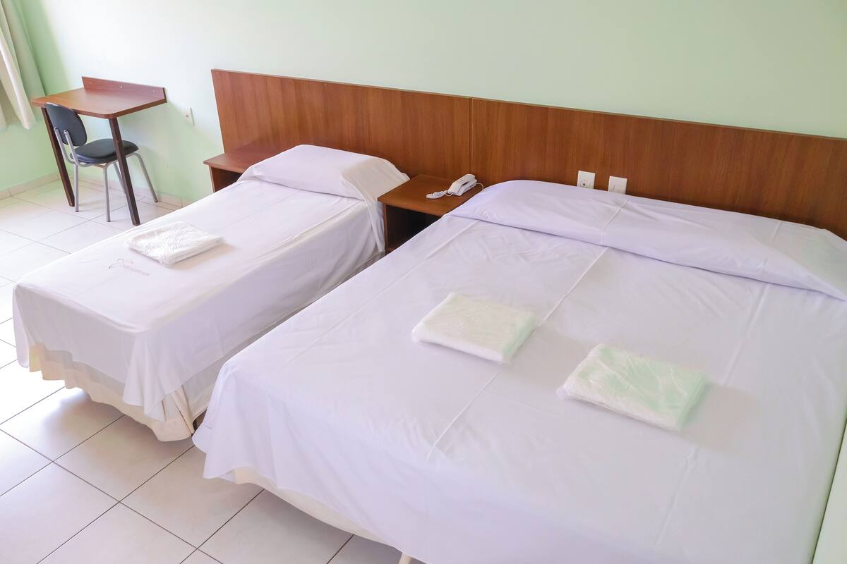 Two single beds with white linens, a wooden nightstand with a telephone, and a small desk with a chair.