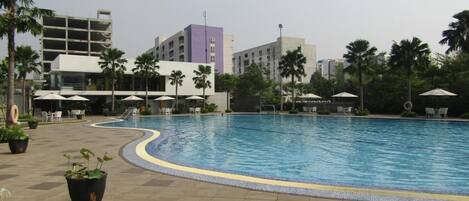 A swimming pool with a tiled edge, surrounded by palm trees and outdoor seating with umbrellas.
