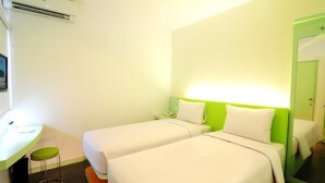 A hotel room with two beds, a desk, and a chair. There is an air conditioning unit above the desk and a green door to the right. - Swift Inn Aeropolis Airport (Tangerang)