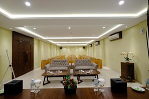 A conference room with a stage, rows of chairs, two sofas, tables with water bottles, and a potted plant. - Pavilliun Seulawah (Banda Aceh)