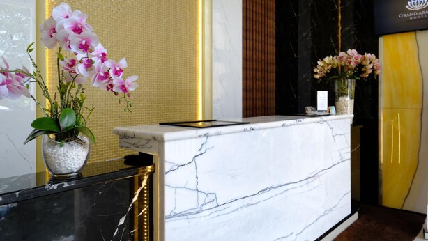 Ein мраmorerer Empfangstresen mit Namensschild, eine Vase mit Blumen und eine strukturierte Wand im Hintergrund.