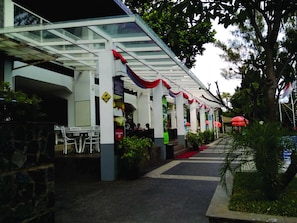 A covered outdoor seating area with tables and chairs, a red carpet, and potted plants.