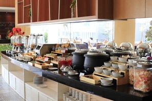 Buffet com diversos alimentos e bebidas, incluindo tigelas, pratos e recipientes.