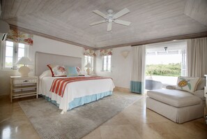 Quarto com cama, mesa de cabeceira, janela e ventoinha no teto, além de vista para o verde lá fora.