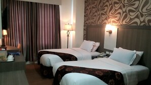 Une chambre d’hôtel avec deux lits, un bureau, une lampe et un mur décoré d’un motif.