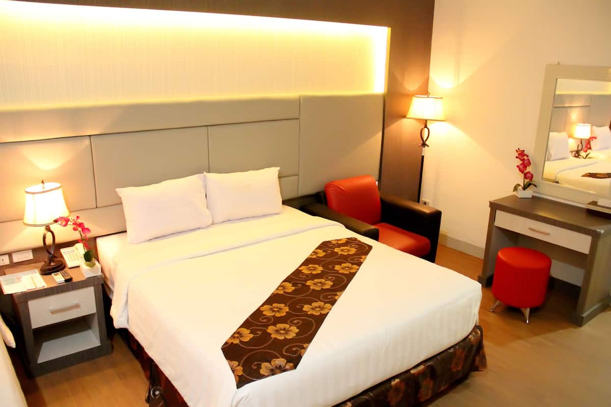 Una habitación de hotel con una cama, un escritorio, una silla y una mesita de noche con lámpara.