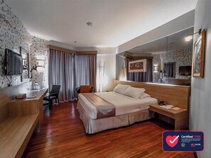 A hotel room with a bed, desk, chair, and a large mirror. - Klub Bunga Butik Resort (Batu)