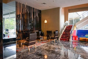 Un vestíbul de disseny modern, amb un paviment de marbre, una escala amb alfàbbra vermella i una zona de seients amb cadires i taules.