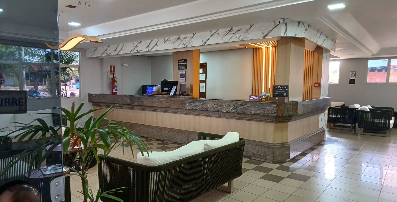 A hotel reception area with a marble counter, a reception desk, a seating area with a sofa and chairs, and a potted plant.
