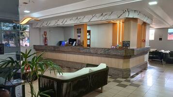 A hotel reception area with a marble counter, a reception desk, a seating area with a sofa and chairs, and a potted plant.