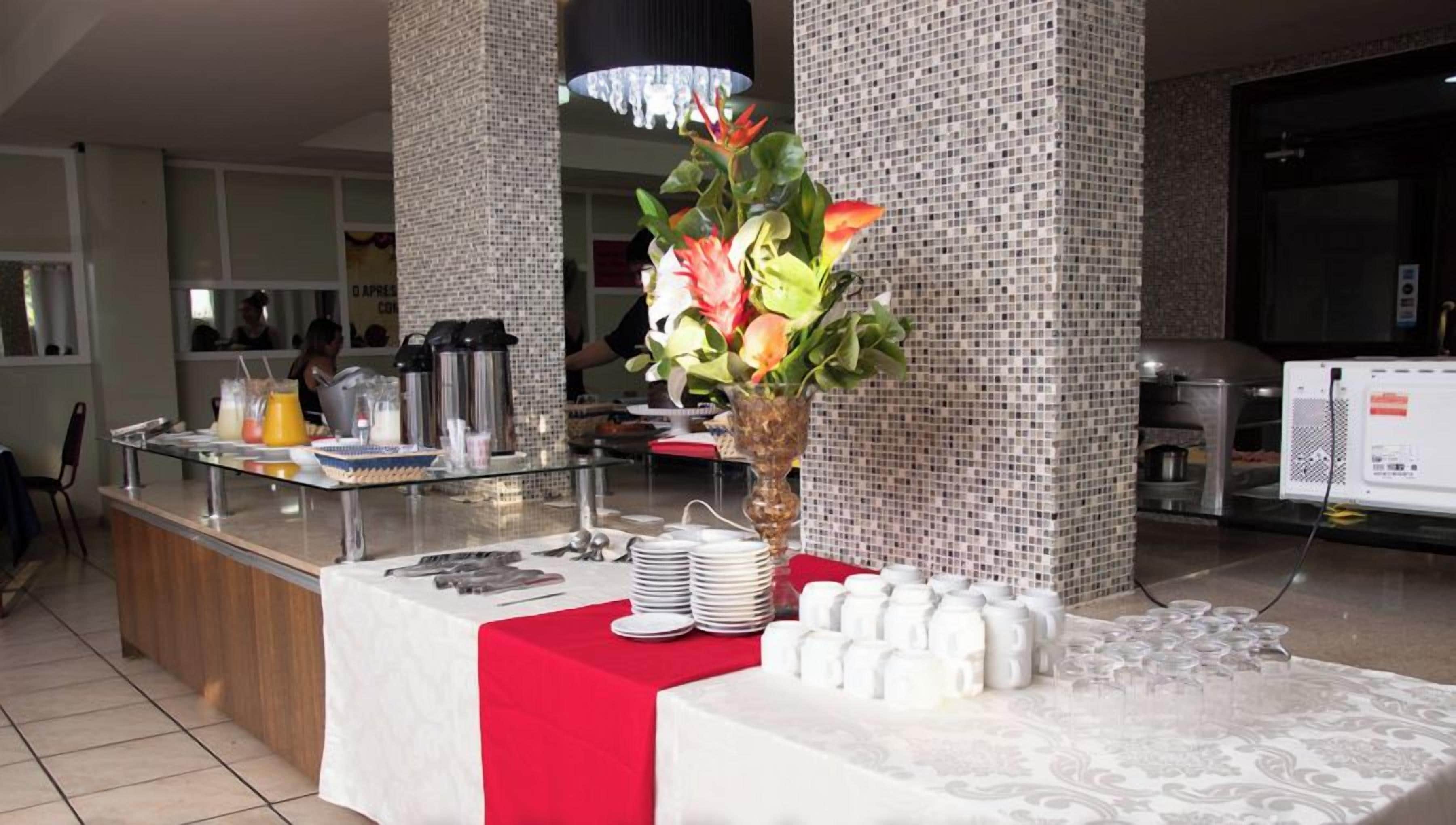 A buffet setup with a red tablecloth, a vase of flowers, and various food and drink containers.