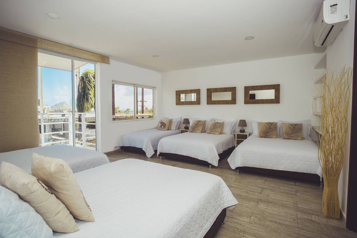 A hotel room with three beds, a large window, and a view of the city.