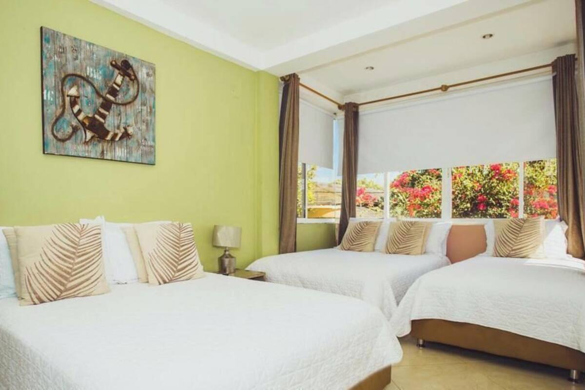 A hotel room with two beds, a painting on the wall, and a window with a view of greenery.
