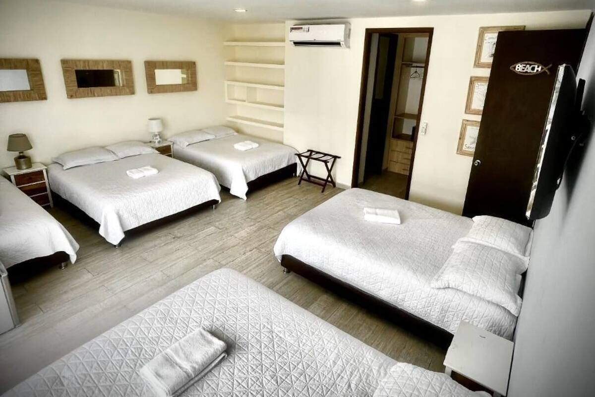 A hotel room with four beds, a small table, a wardrobe, and an air conditioning unit.