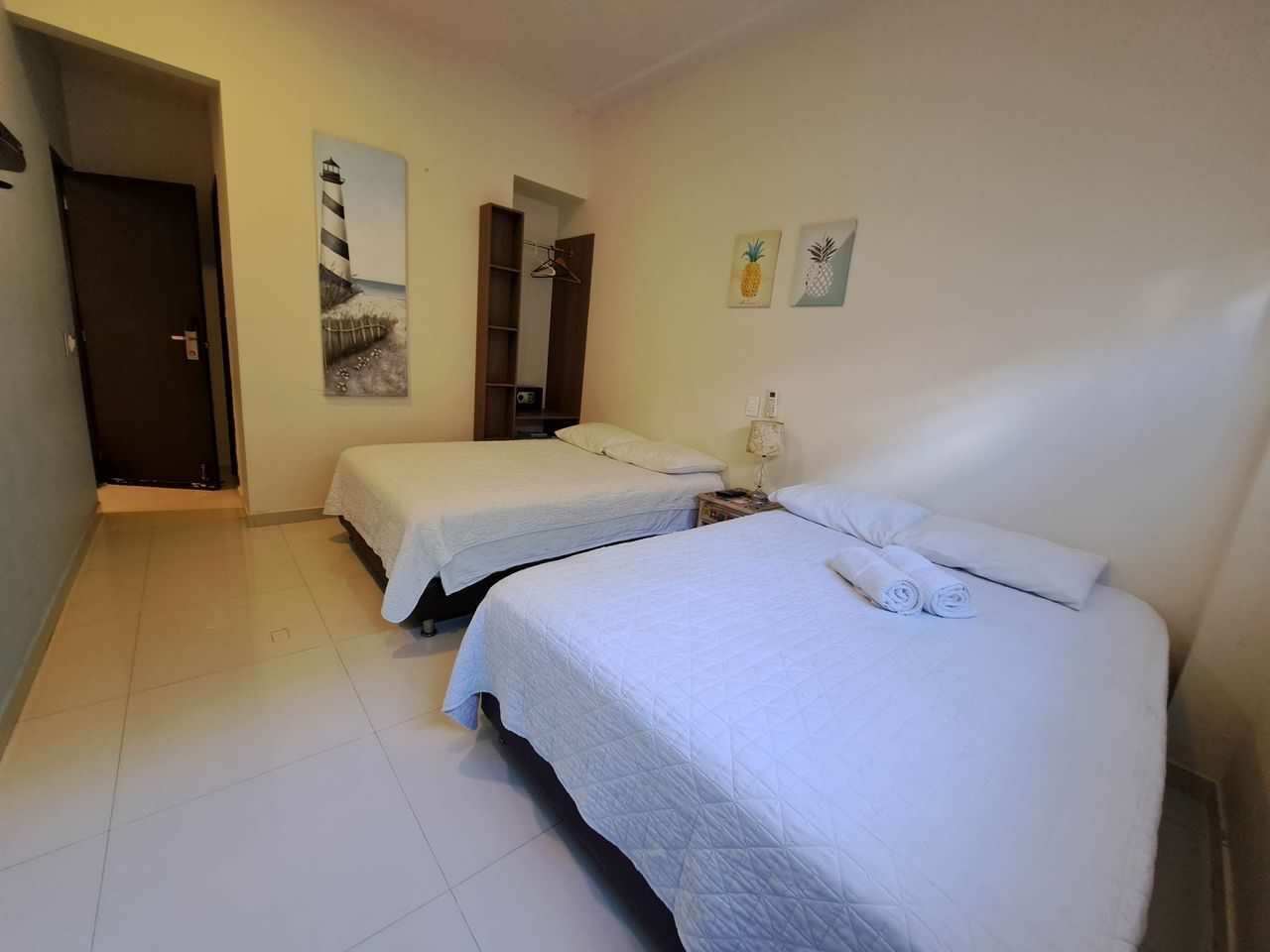 A hotel room with two beds, a wardrobe, a mirror, and artwork on the walls.