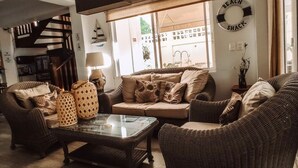 A living room with a sofa set, a coffee table, and a lamp. There is a window with a view of the outside, a wall clock, and a sign that reads "BEACH SHACK". - Summer House Inn San Andres (San Andrés)