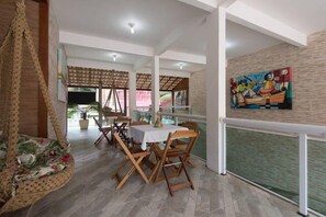 A dining area with a table and chairs, a hanging chair, and a painting on the wall. - Recanto da Sofia (Búzios)