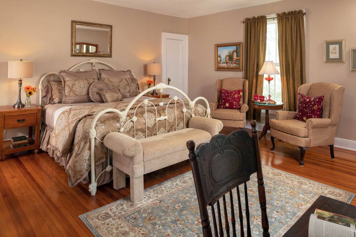 A bedroom with a bed, a chair, a nightstand, a lamp, and a small table with a lamp.