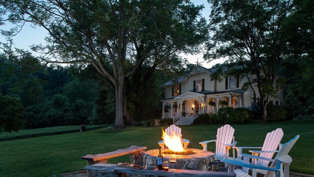 A fire pit with Adirondack chairs and a stone table in a garden setting. - Orchard House B&B (Lovingston)