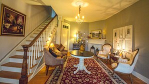 A spacious living room with a grand staircase, a chandelier, and a fireplace. - Orchard House B&B (Lovingston)