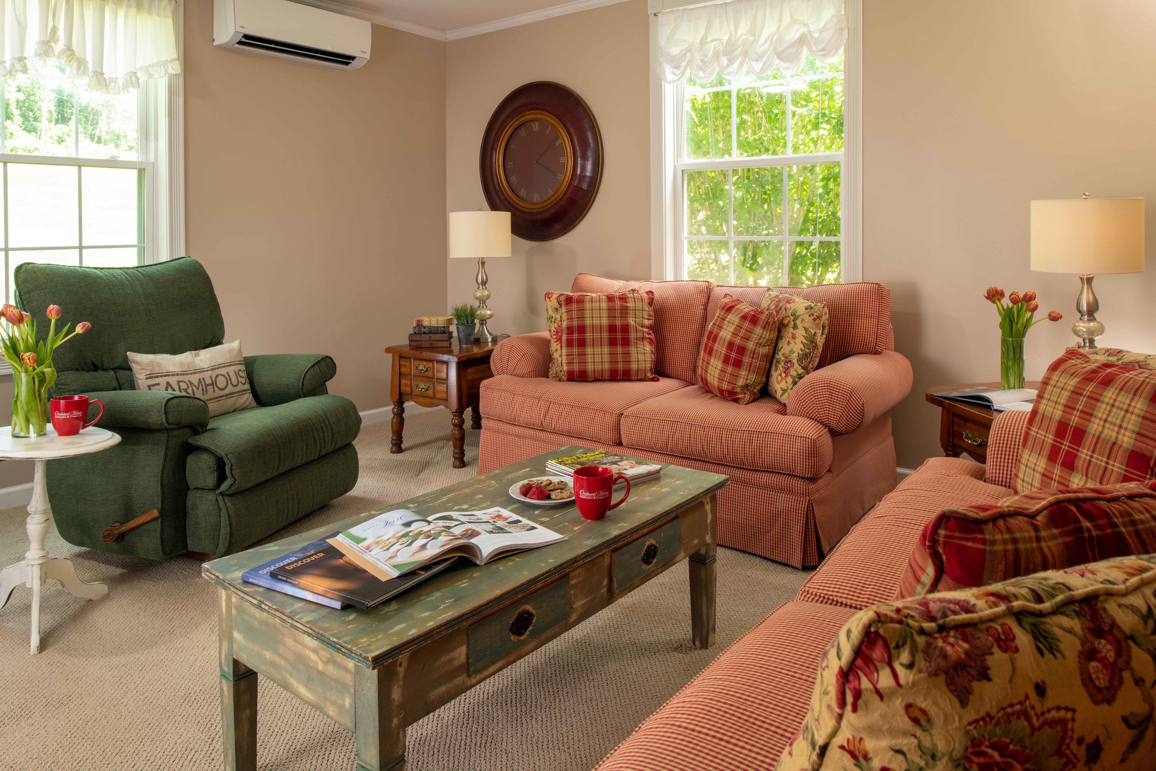 A cozy living room with a green armchair, a plaid sofa, and a wooden coffee table with magazines.