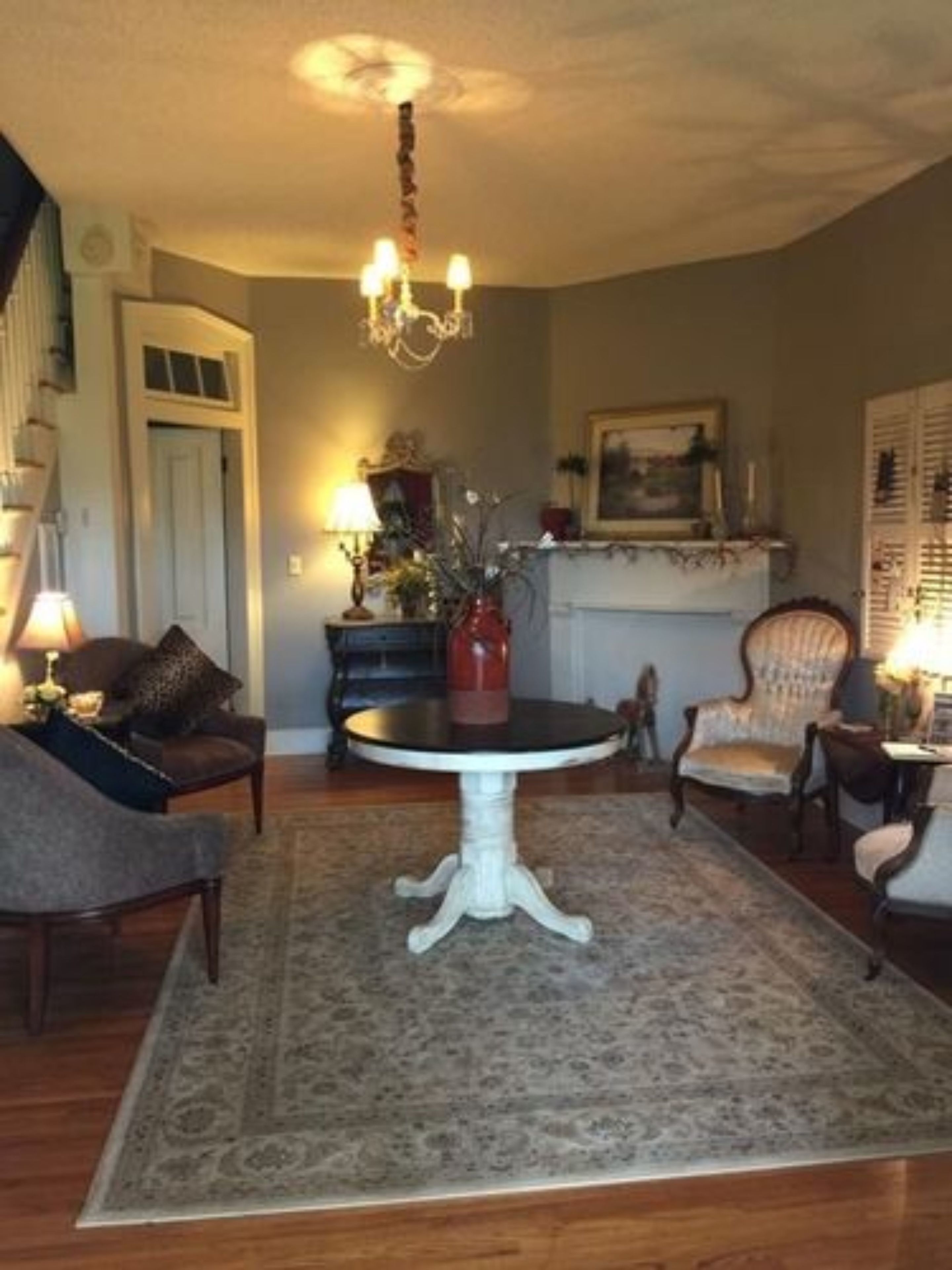 Un salon avec une table ronde, deux fauteuils, un canapé, un lustre et une cheminée.