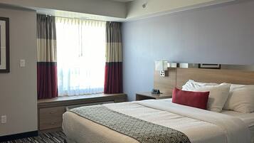 Hotelkamer met een groot bed, nachtkastje met lamp, raam met gordijnen en een plafondlamp.