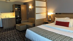 A hotel room with a bed, a sofa, a desk with a lamp, a minibar, and a ceiling light. - Microtel Inn & Suites by Wyndham Sudbury (Sudbury)