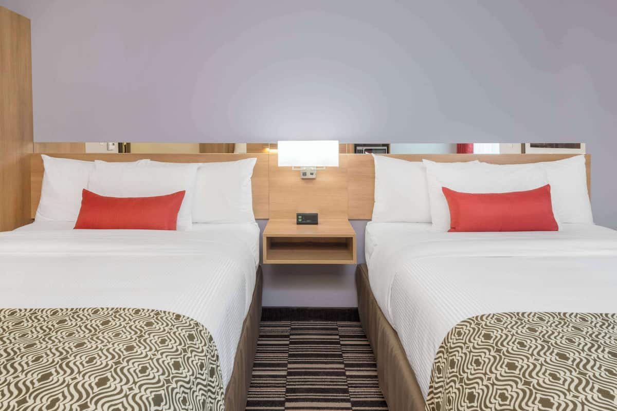 Une chambre d’hôtel avec deux lits, une table de chevet, une lampe et un tapis à motifs.