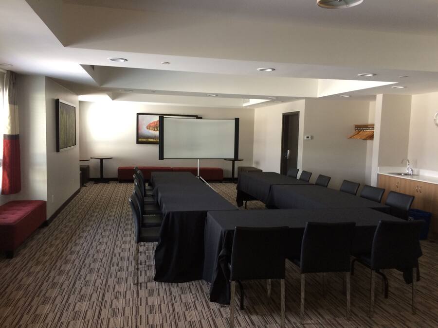 Ein Konferenzraum mit einem langen Tisch, Stühlen, einer Projektionsleinwand und einer kleinen Sitzecke.